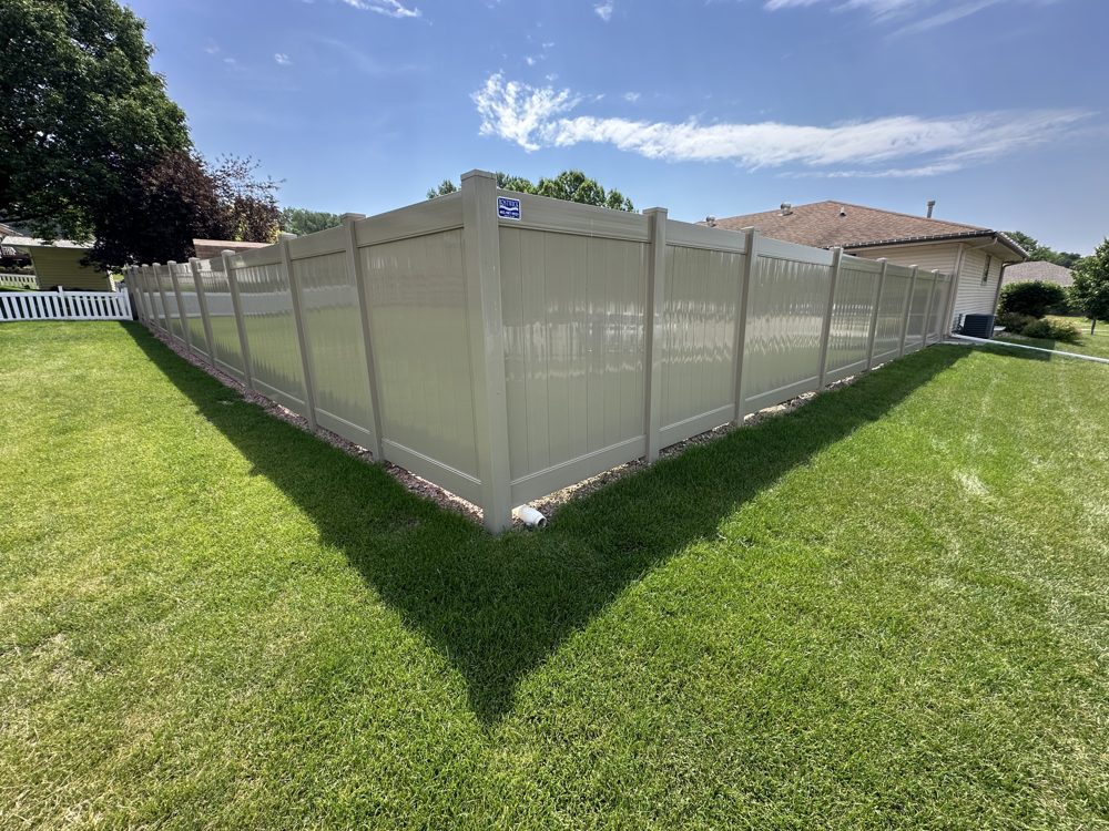 Tan vinyl privacy fence installed around a back yard